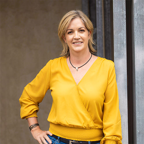 Blonde woman in yellow shirt, smiling confidently at the camera